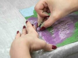 Hand is in motion. Drawing with pastels close-up. Woman drawing beautiful crocus flowers with soft pastel at table. Close up. photo