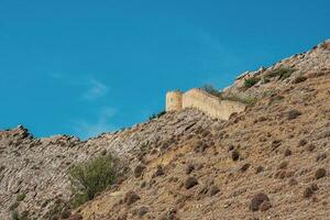 The wall of the old fortress on the hill against the blue sky. Gunib fortress is a historical monument of Dagestan. photo