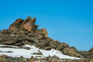 Sharp rocks. Highland scenery with sharpened stones of unusual shape. Awesome scenic mountain landscape with big cracked pointed stones closeup among snow under blue sky in sunlight photo