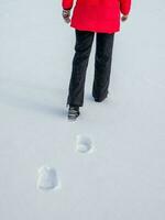 Woman in the red jacket walking on snow, footprints in snow, behind photo