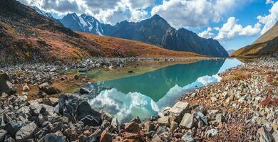 Amazing clean mountain lake in a high-altitude valley. Beautiful nature of Altai mountains. Lake in the valley, rocks and snow. Wonderful summer sunny day with gorgeous cloudscape. photo