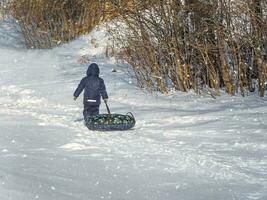 Boy with tubing rises to the mountain. Child having fun on snow tube photo