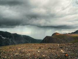 Rainy alpine view from stone hills to high mountain range in sunlight during dramatic in changeable weather. photo