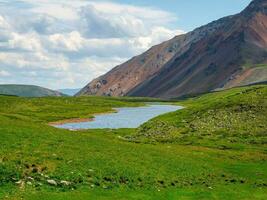 Colorful summer landscape with beautiful lake in sunlit green mountain valley among rocks and high mountain ridge under blue sky. Awesome scenery with alpine lake among greenery in sunlight. photo