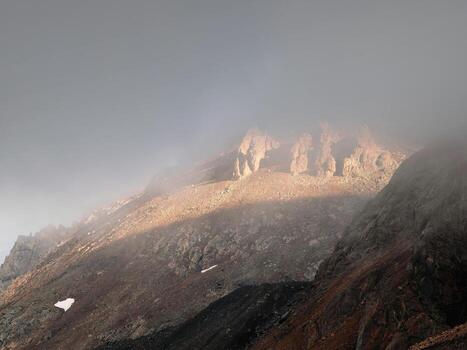 Atmospheric ghostly landscape with fuzzy silhouettes of sharp rocks in low clouds. Dramatic view to large mountains blurred in rain haze in gray low clouds. Diagonal slope of the mountain photo