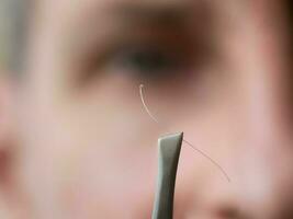 Tweezers with gray hair in front of the woman face. photo