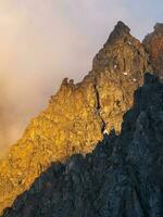 Scenic landscape with golden light in mountain top in low clouds in yellow sunrise colors. Colorful view to mountains and rocks in morning sunlight in low clouds. Bright scenery with golden rocks. photo