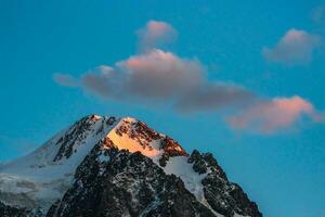 parte superior negro rocas en noche dorado Brillo Solar y nieve blanca puntiagudo cima. atmosférico amanecer paisaje con alto Nevado montaña con puntiagudo cima. foto