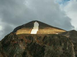 Caldera is flooded with sunlight. Landscape with sunlit wide sharp mountain ridge between mountain tops. Colorful mountain scenery with large sharp rocks on ridge top in sunlight under cloudy sky. photo