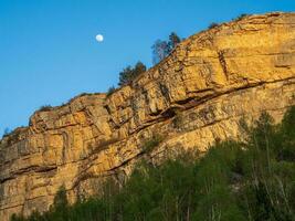 White moon is above the rock. Rock against the evening blue sky. High peaked sharp rock. Rocky sharp mountain ridge with a chasm. photo