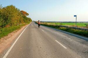 Solo journey concept. Back view of woman with backpack walking on autumn country road, hiking trip photo