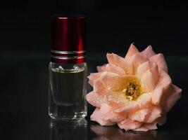 Concentrated perfume in a mini bottle with pink scented tea rose on the black background photo