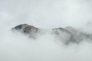 maravilloso minimalista paisaje con grande Nevado montaña picos encima bajo nubes atmosférico minimalismo con grande nieve montaña tapas en nublado cielo. foto