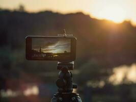 de cerca teléfono inteligente tomar un paisaje foto y vídeo lapso de tiempo en estar trípode en puesta de sol