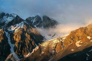 Scenic landscape with golden light in mountain top in low clouds in yellow sunrise colors. Colorful view to mountains and rocks in morning sunlight in low clouds. Bright scenery with golden rocks. photo