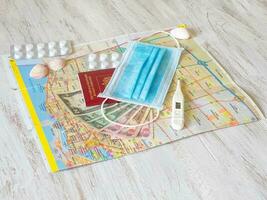 A medical mask, map, pills, passport, and money are laid out on the table. Travel concept photo