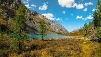 Panoramic alpine landscape with mountain lake in green valley in summer under blue sky. Awesome highland scenery with beautiful glacial lake among sunlit hills and rocks against mountain range. photo