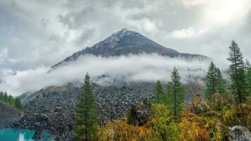 panorámico ver de el otoño montaña, un estrecho tira de niebla terminado el montaña pendientes en el distancia, blanco nubes relleno el montaña garganta. un claro azul montaña lago y un brillante otoño bosque. foto