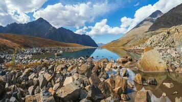 Panoramic view of the autumn mountain lake with reflection white clouds. A clear blue mountain lake and a bright autumn stones floating in water. photo