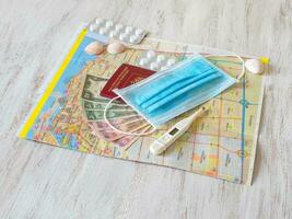 A medical mask, map, pills, passport, and money are laid out on the table. Travel concept photo