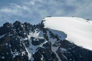 nieve repisa en el parte superior de el montaña. repisas desde el Nevado montañas. acantilados y grande rocas peligroso terreno. foto