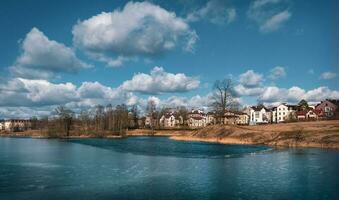 Eco-friendly cottage village on the shore of the lake. Bright spring landscape with houses near a frozen lake. photo
