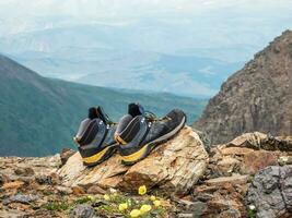 Wet hiking boots dry on a stone against the background of snow-covered high mountains. The difficulties of hiking, drying clothes in nature. photo