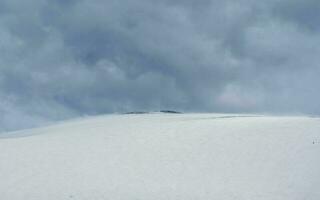 Selective focus. Snowy haze, poor visibility. Snow mountain dome. Big snowy mountain under gday dramatic cloud. photo