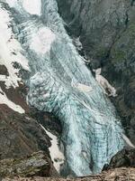 vertical montaña paisaje con azul largo vertical glaciar lengua con grietas entre rocas aéreo ver a grande glaciar con caida de hielo. naturaleza textura de montaña glaciar con fisuras cerca arriba. foto