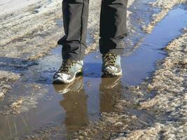 Trekking boots in the muddy spring. The ice melts in the spring, a man walks through puddles on the street, spring weather photo