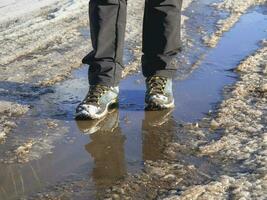 trekking botas en el lodoso primavera. el hielo se derrite en el primavera, un hombre camina mediante charcos en el calle, primavera clima foto