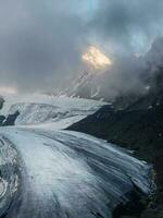 crepúsculo montañas. ligero en el glaciar. majestuoso glaciar es iluminado por el brillante dorado noche Dom. vertical vista. grande aktru glaciar, altai montañas. foto