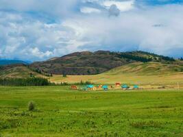 Collective camping to the distance, tourist complex, wooden guest houses against the background of green hills. Farmstead in the steppe. Countryside in highlands. photo