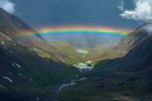 arco iris terminado un montaña valle. atmosférico alpino paisaje con Nevado montañas con arco iris en lluvioso y soleado clima. foto