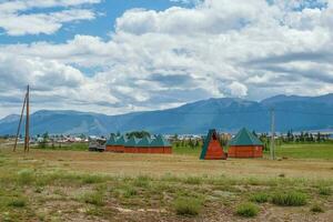 colectivo cámping a el distancia, turista complejo, de madera invitado casas en contra el antecedentes de verde sierras. alquería en el estepa. campo en tierras altas. Kurai aldea. Siberia, altai. foto