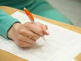 Woman signing document, close up on female hand holding pen and paper on table. Selective focus. photo