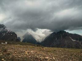 Awesome dark cloud at the top of the mountain. Wonderful dramatic landscape with big snowy mountain peaks above low clouds. Atmospheric large snow mountain tops in cloudy sky. photo