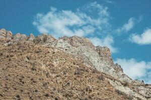 Minimalistic atmospheric landscape with rocky mountain wall with pointy top in sunny light. Loose stone mountain slope in the foreground. Sharp stony mountains. photo