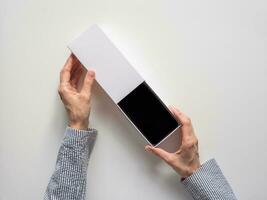 Unpacking a new smartphone on a white table. Female hands holding modern smartphone with blank screen. Online shopping concept. photo