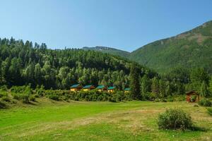 Collective camping with a green lawn in an eco-friendly green place. Summer tourist complex, wooden guest houses against the background of fir-covered high mountains. photo