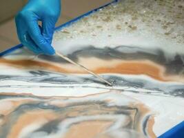 Technology process of creating a painting in style resin art, woman works with epoxy in studio,  makes a wooden stand with the image. Epoxy resin art painting space. photo