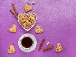 Festive ginger cookies with cinnamon in the shape of hearts are laid out on a pink background. Top view. photo