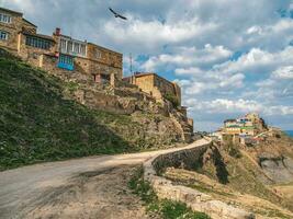 Sandy winding road to the mountain village. Sunny view of villade on the rock. Authentic Dagestani mountain village of Choh. Russia. photo