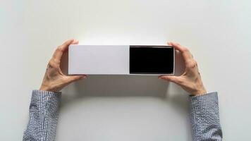 Unpacking a new smartphone on a white table. Female hands holding modern smartphone with blank screen. Online shopping concept. photo