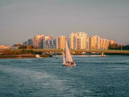 A yacht with sails drifts on the river against the background of a residential neighborhood with high-rise buildings. Saint-Petersburg. photo