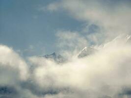 Wonderful minimalist landscape with big snowy mountain peaks above low clouds. Atmospheric minimalism with large snow mountain tops in cloudy sky. photo