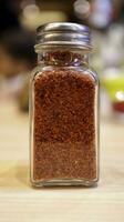 A small glass bottle of dried red chili pepper for condiment or seasoning. photo