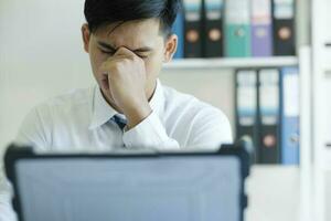 Tired and overworked manager sitting in front of computer and trying to concentrate, his eyes are dry and hurt. photo
