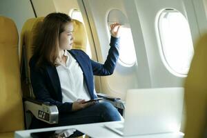 Business woman In a plane, works on using laptop computer and phone, look in the plane window. photo