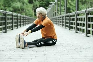 Athletic Senior woman stretching two legs in park. photo